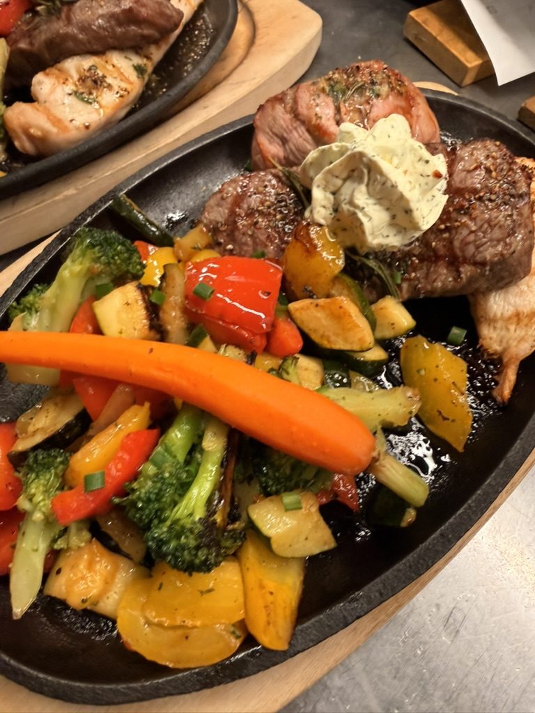 Grillpfanne mit Fleisch vom Grill, Kräuterbutter und buntem Gemüse in der gusseisernen Pfanne